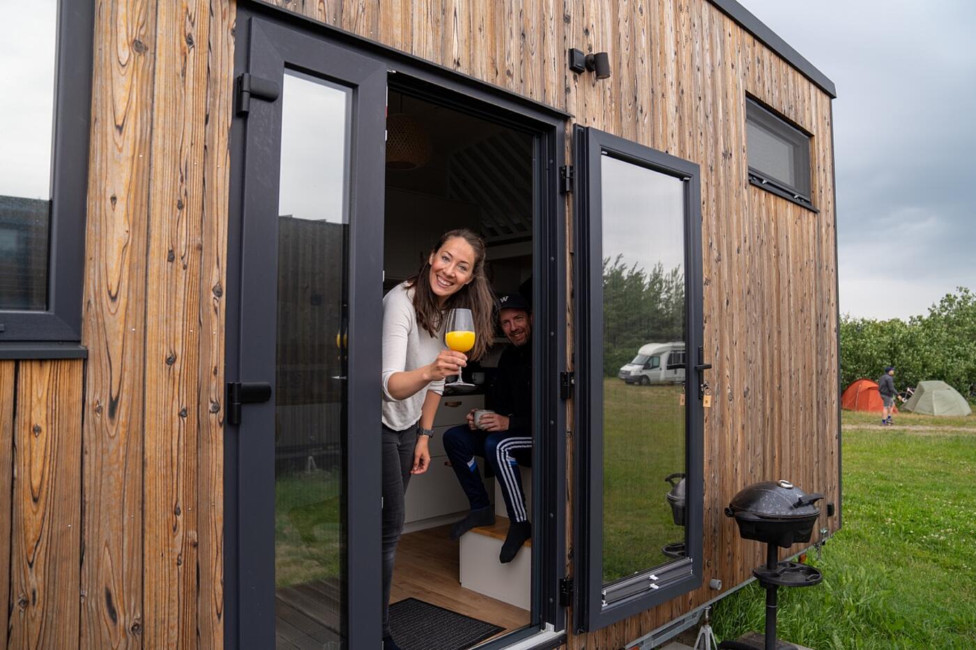 Blick auf ein Tiny House, aus dessen offener Tür zwei Teammitglieder von visuellverstehen fröhlich herausschauen.