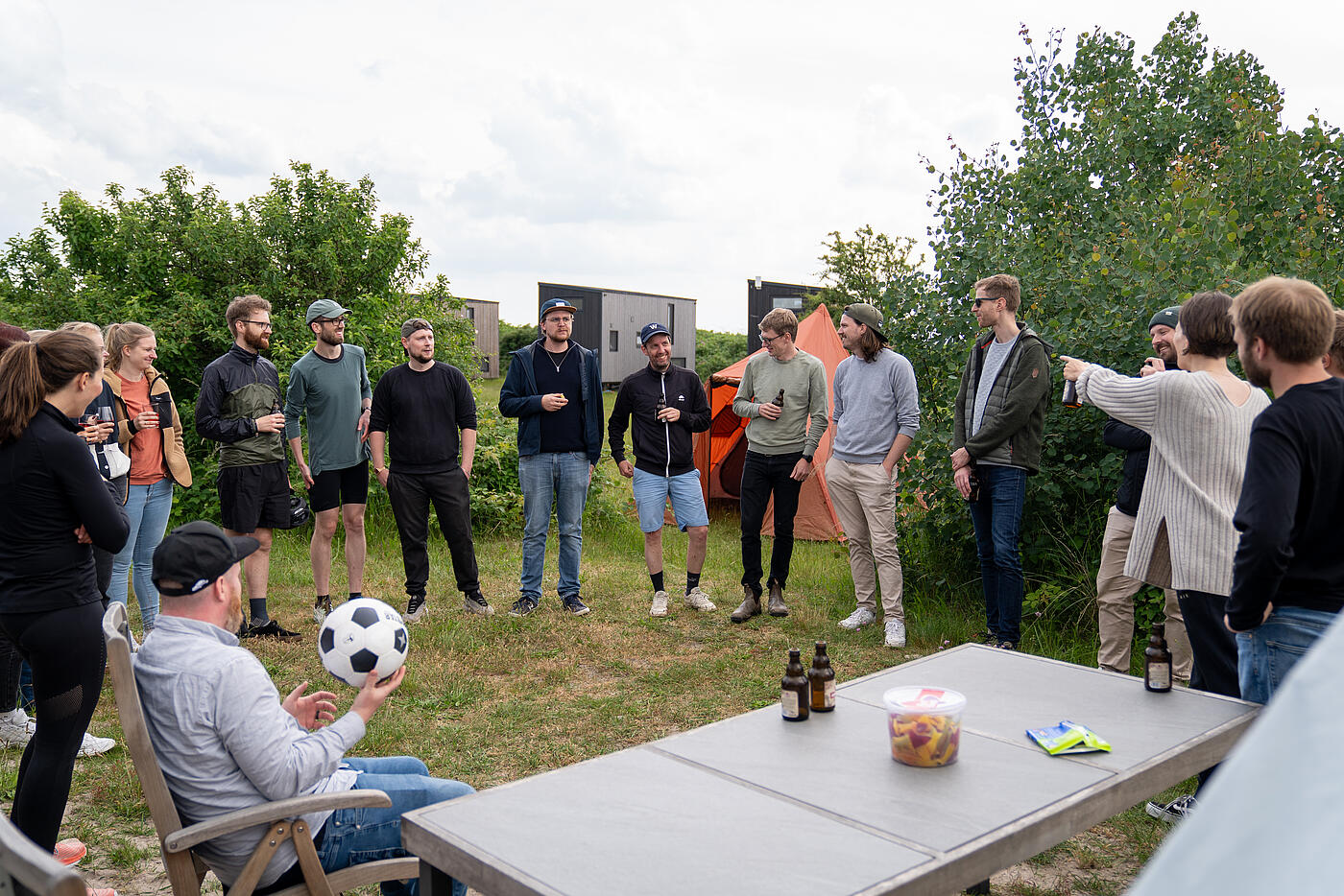 Das Team von visuellverstehen steht im Kreis vor einem Campingtisch im Grünen. Viele lachen.