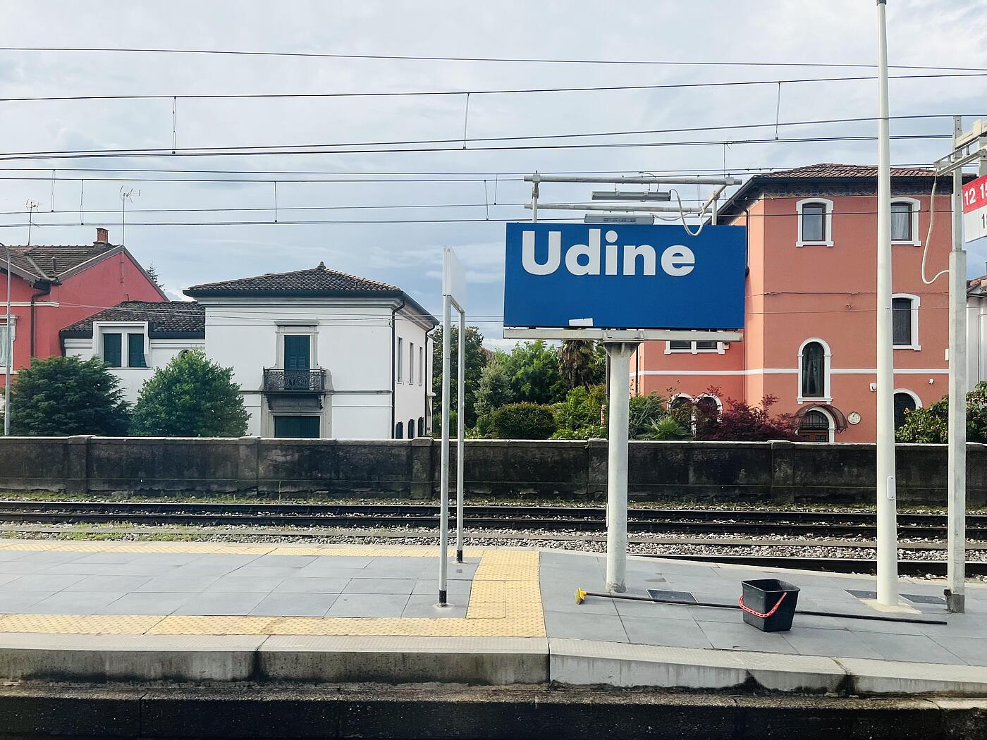 Bahnsteig mit blauem Schild auf dem in weißer Schrift Udine steht.