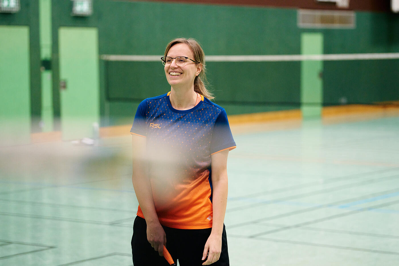Eine Mitarbeiterin von visuellverstehen spielt Badminton in einer Turnhalle.