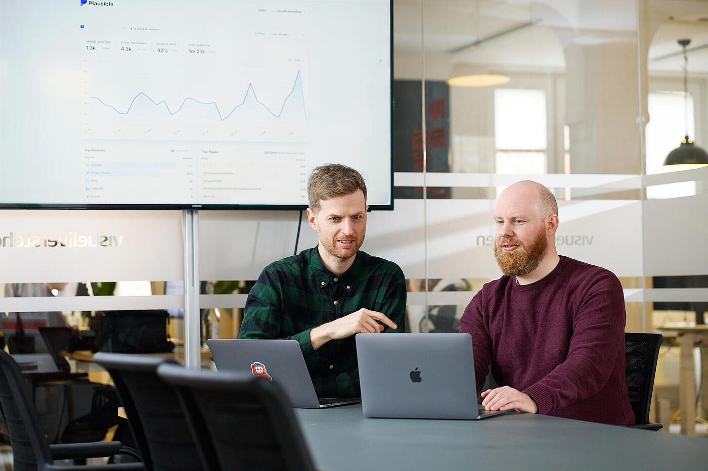 Zwei Mitarbeiter von visuellverstehen sitzen vor ihren Macbooks und besprechen etwas.