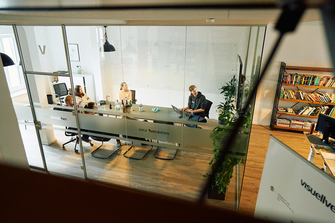 Blick in den verglasten Besprechungsraum von visuellverstehen, in dem mehrere Mitarbeitende sitzen.