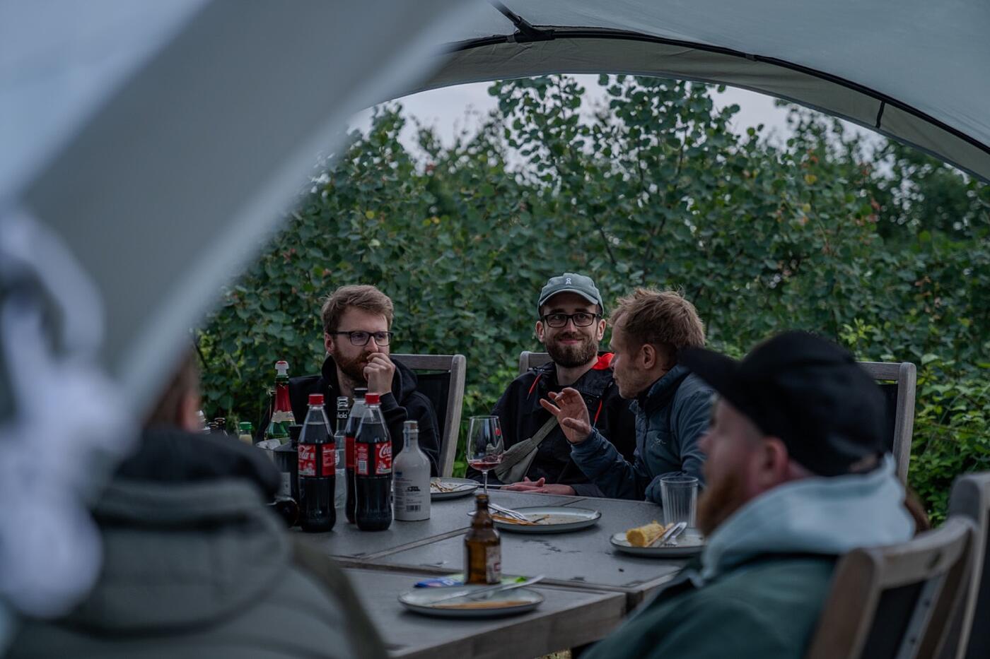 Vier Teammitglieder von visuellverstehen sitzen abends unter einem Pavillon im Freien an einem Tisch.