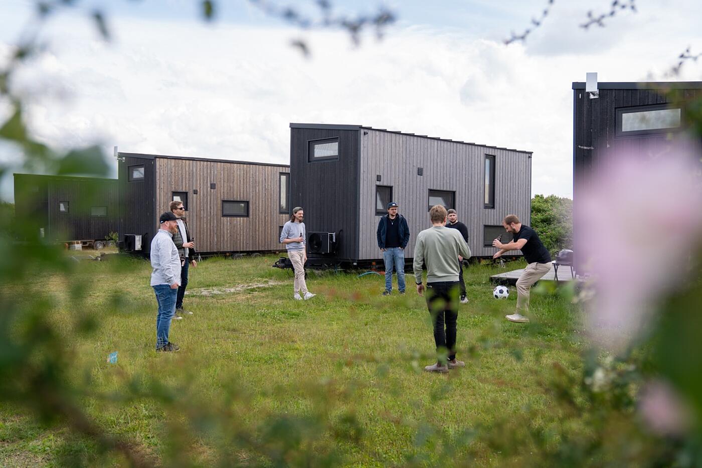 Mehrere Mitarbeiter von visuellverstehen spielen draußen zwischen den Tiny Houses Fußball.