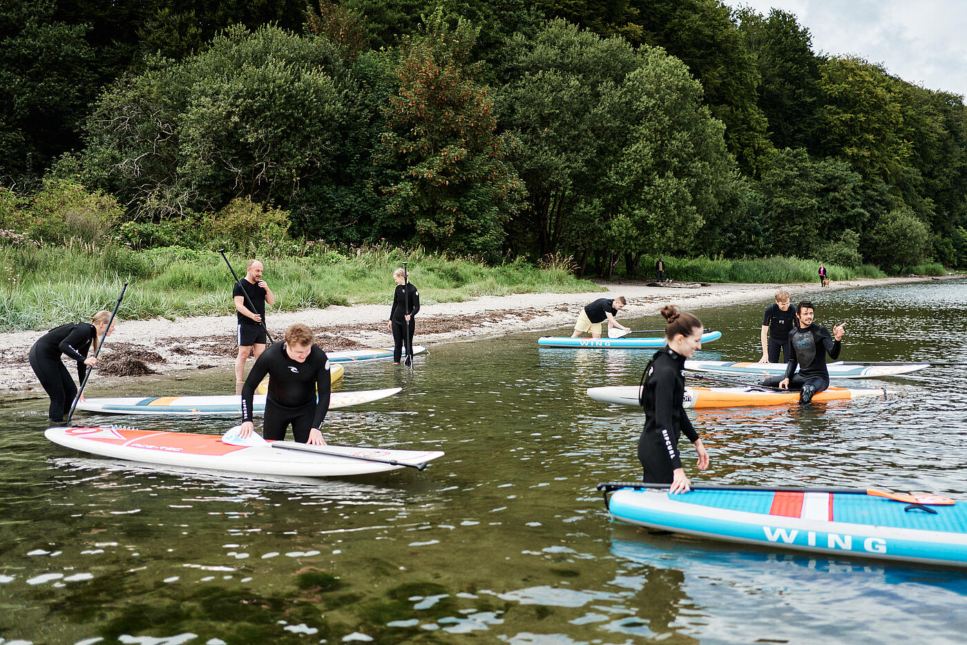 Beim Sommerfest gehen mehrere Mitarbeitende von visuellverstehen vorm Flensburger Ruderklub mit ihren Kajaks ins Wasser. 