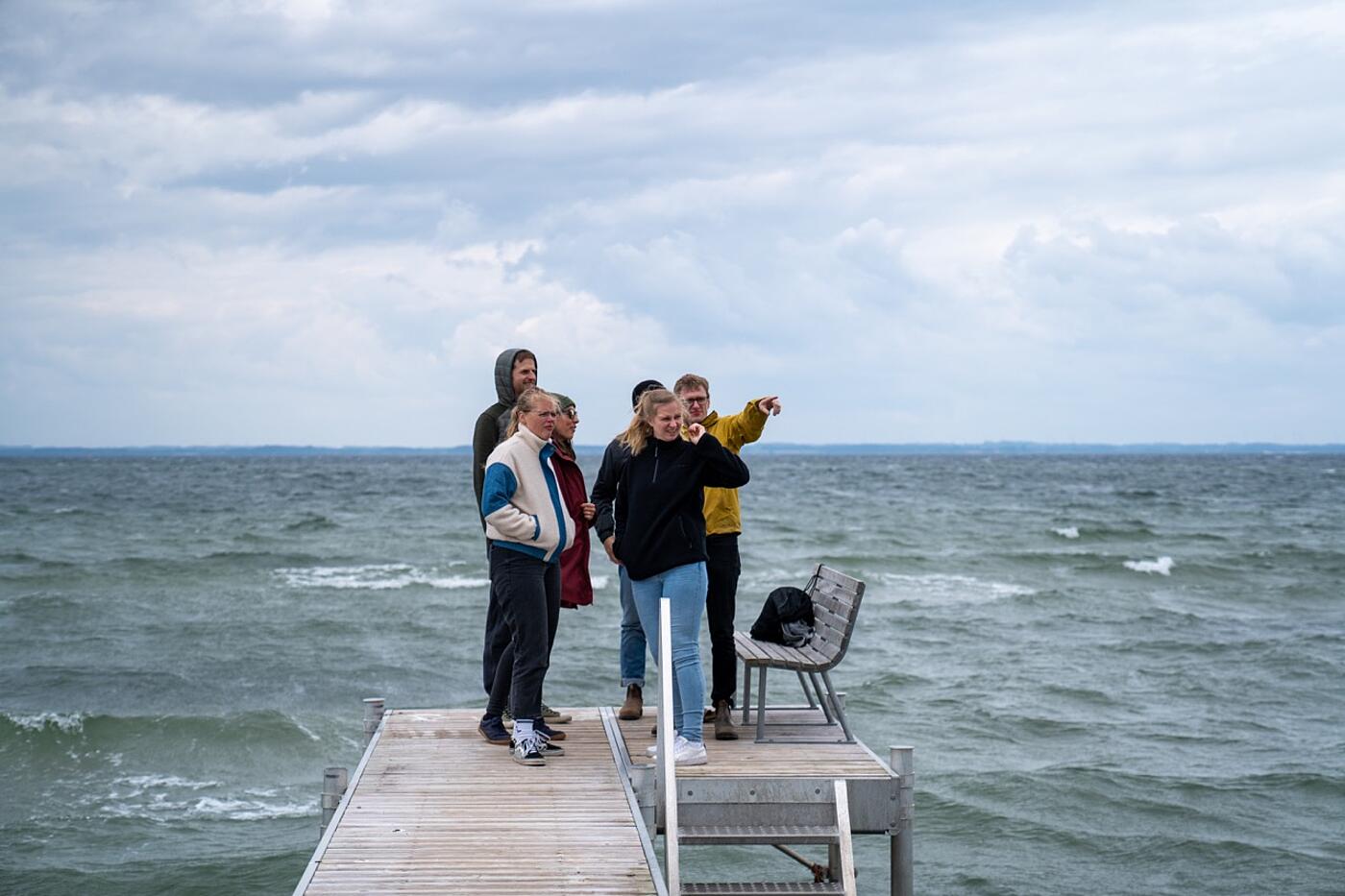 Vier Teammitglieder von visuellverstehen auf einem Holzsteg, der ins Meer hineinragt.