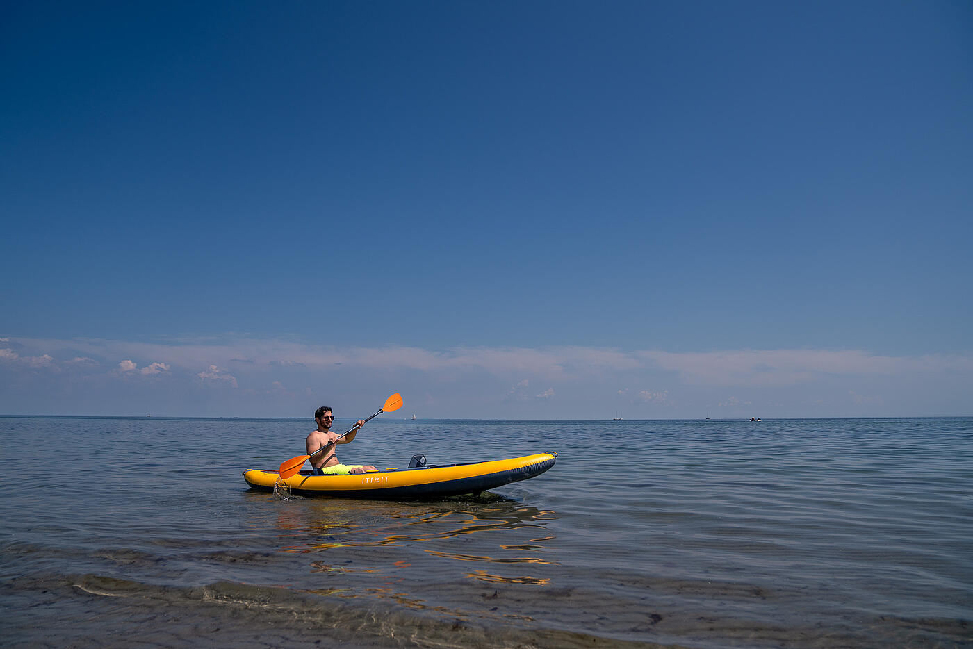 Ein Mitarbeiter von visuellverstehen paddelt in seinem Kanu vor blauem Himmel und Meer.