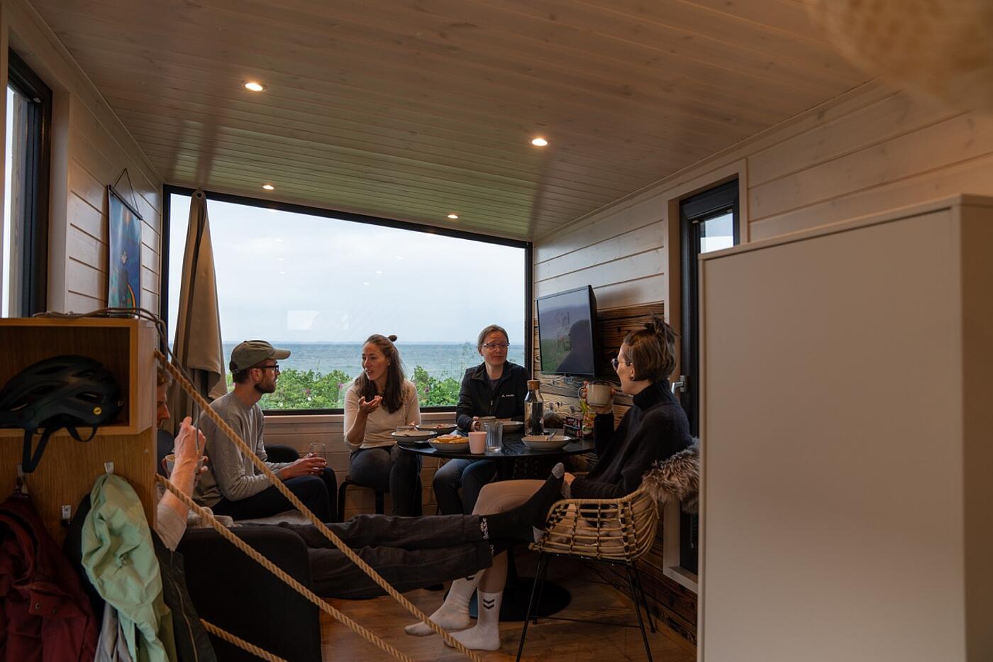 In einem Tiny House mit Blick aufs Meer sitzen mehrere Teammitglieder von visuellverstehen zusammen.