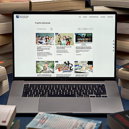 Ein aufgeklapptes Macbook zeigt den neuen Internetauftritt der Büchereizentrale SH inmitten von Bücherstapeln auf einem Tisch.