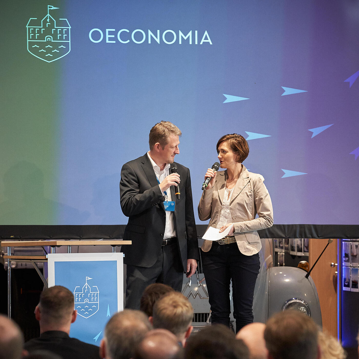 Zwei Personen stehen auf der Bühne der Oeconomia 2018 und halten Mikrofone in der Hand.