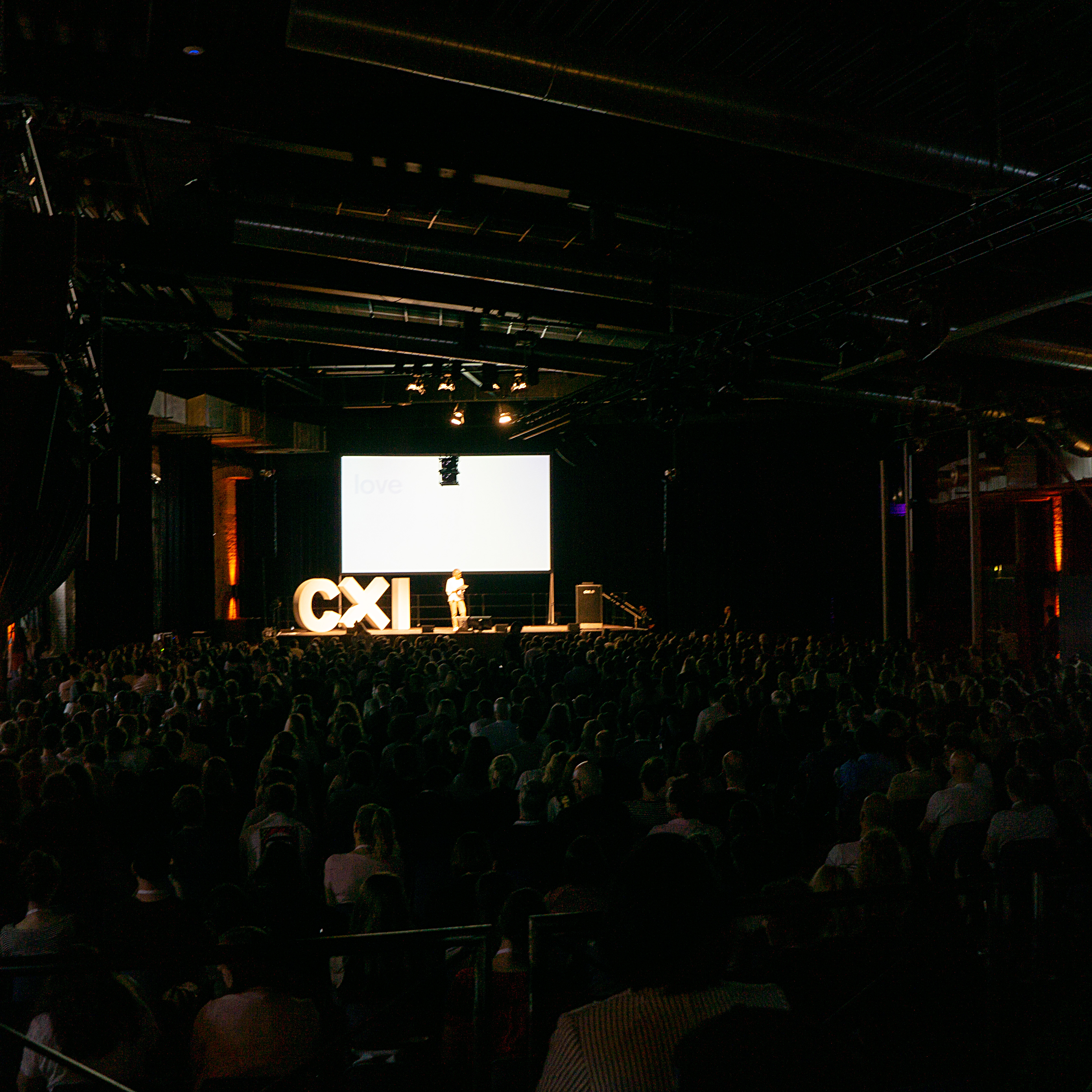 Ein vollbesetzter, dunkler Saal mit einer hell erleuchteten Bühne bei der CXI-Konferenz in Berlin.