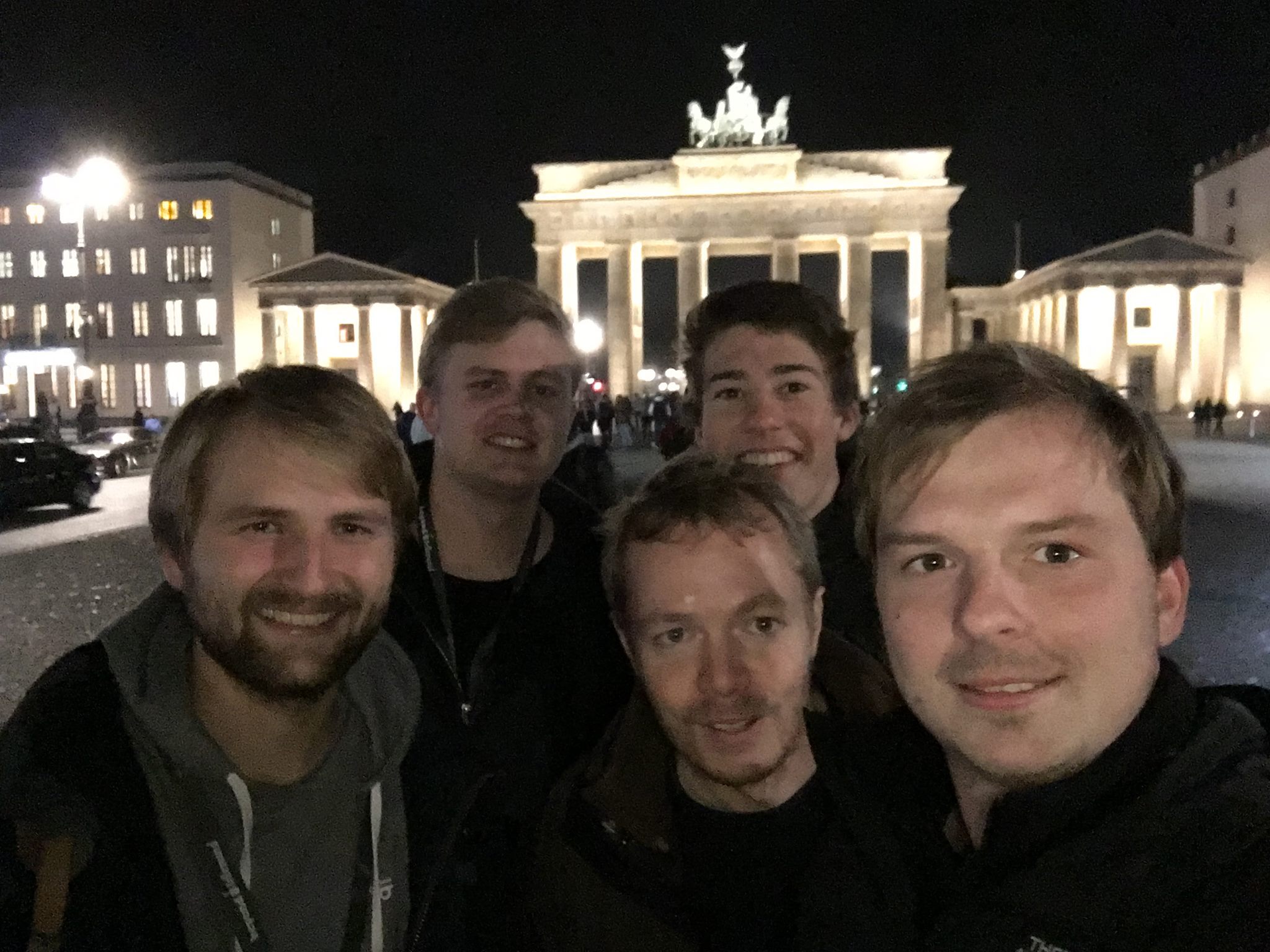 Mehrere Mitarbeiter von visuellverstehen stehen vor dem Brandenburger Tor und schauen in die Kamera. Es ist Nacht.