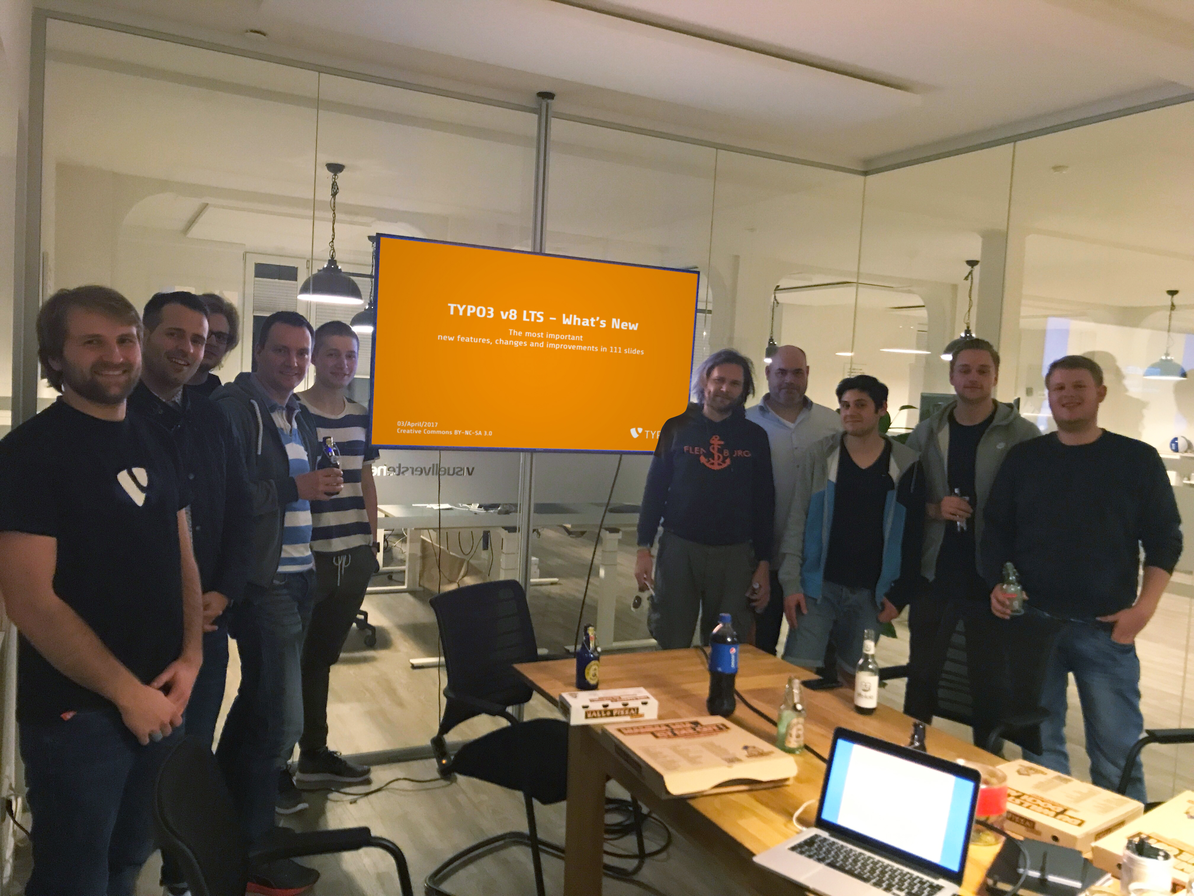 Das Team von visuellverstehen posiert in einem verglasten Besprechungsraum vor einem orangen Bildschirm mit einer Typo3-Überschrift.